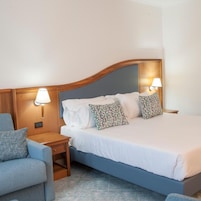 A hotel room with a bed, two bedside lamps, a nightstand, and a chair.