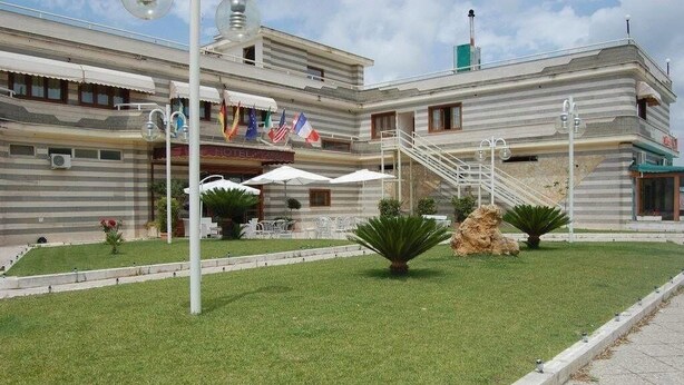 Un hotel con techo plano, varios pisos y una escalera central. Hay zonas de estar exteriores con sombrillas.