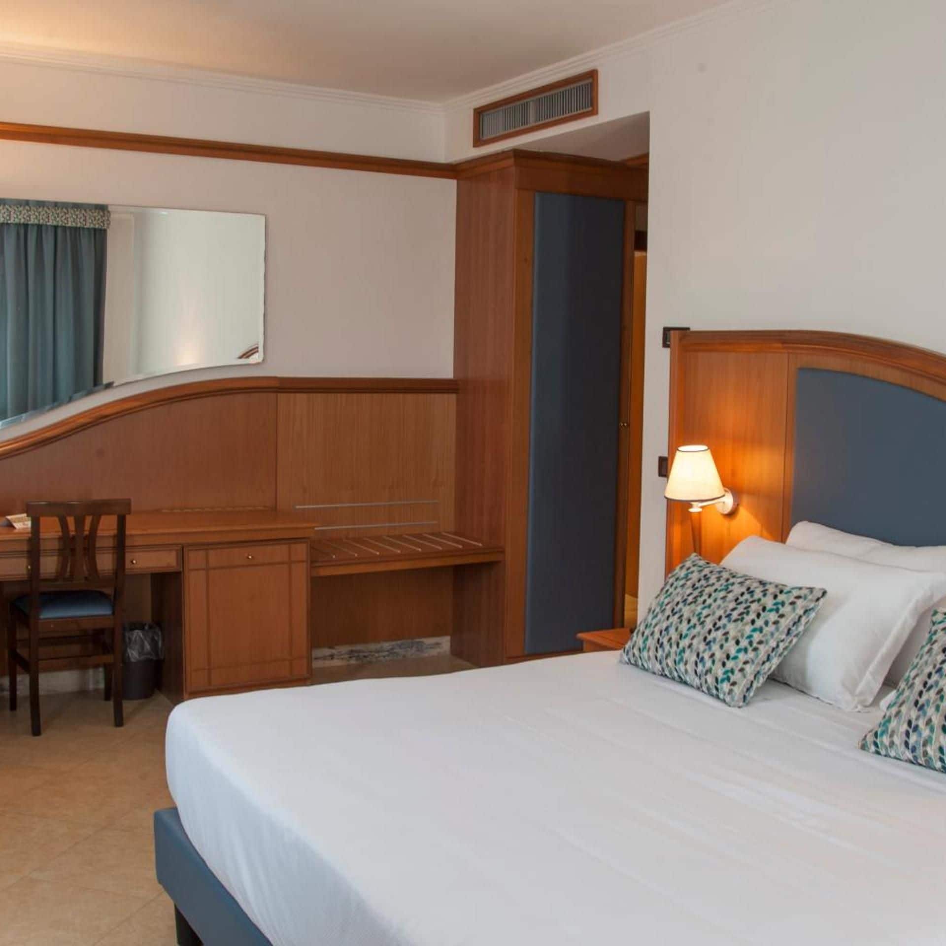 Una habitación de hotel con una cama, un escritorio, una silla, una lámpara y un espejo.