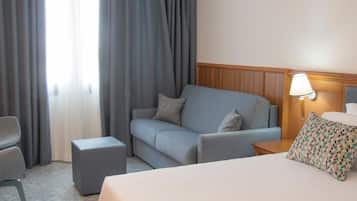 A hotel room with a bed, a sofa, a chair, a nightstand, and a lamp.