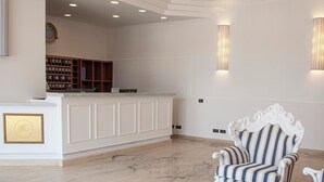 A reception area with a white counter, bookshelves, a clock, and a striped armchair. - Hotel Centrale Sabaudia (Sabaudia)