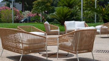 Outdoor wicker furniture arranged in a semi-circle, with a palm tree and flowering plants in the background.