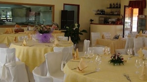 Un salón de banquetes con varias mesas redondas dispuestas para cenar, cada una con sillas blancas y cubertería.
