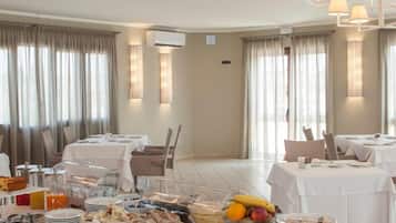 A hotel dining area with tables set for breakfast, including a variety of food items and a buffet.