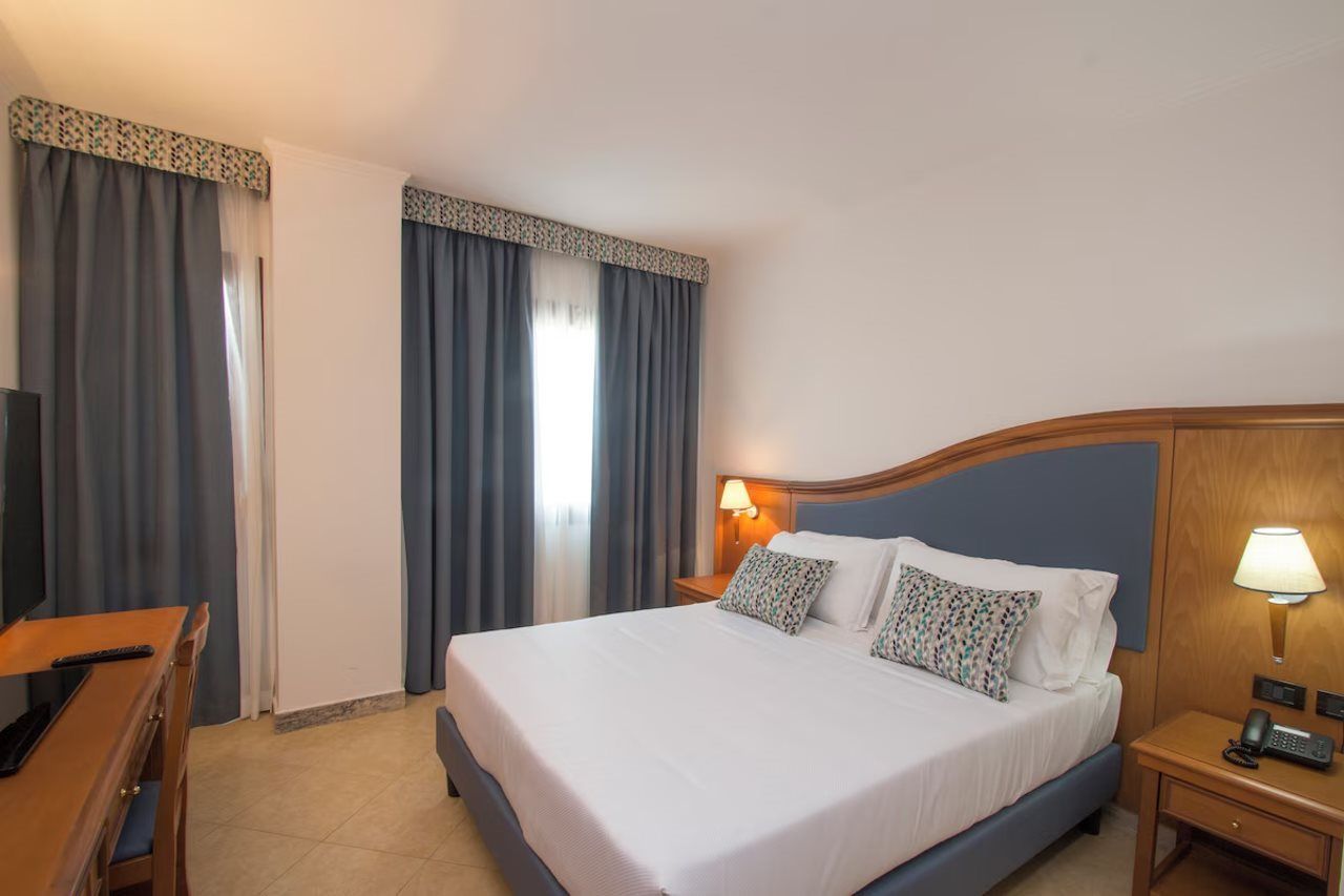 A hotel room with a bed, bedside tables, a desk, and curtains.