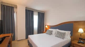 A hotel room with a bed, bedside tables, a desk, and curtains.