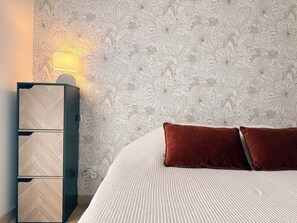 Een slaapkamer met behang met een patroon, een bed met twee kussens en een nachtkastje met een lamp.