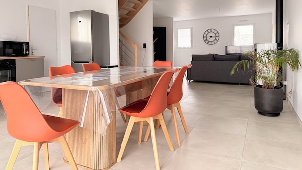A modern kitchen with a microwave, stove, and dining area with a glass table and orange chairs. - The Liberators - Collection La 21ème Planche (Bayeux)