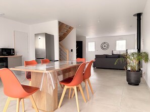 Een moderne keuken met een magnetron, fornuis en een eethoek met een glazen tafel en oranje stoelen.