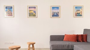 A modern living room with a grey sofa, two wooden stools, a black coffee table, and four framed posters on the wall. - The Liberators - Collection La 21ème Planche (Bayeux)