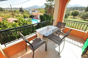 A balcony with a table and chairs, overlooking a pool and greenery.