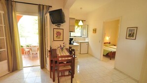 A room with a dining table, chairs, a television mounted on the wall, a bed, and a small kitchenette. - Elena Apartments (Corfu)