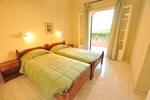 A double bed with a wooden frame and green bedding in a room with tiled flooring and a door leading to an outdoor area. - Elena Apartments (Corfu)