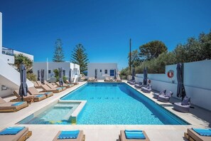 A swimming pool with lounge chairs and umbrellas, surrounded by white buildings. - Cretan Seaside Boutique Hotel (Hersonissos)