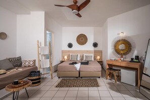 A bedroom with a bed, a desk, a chair, a ceiling fan, and a small refrigerator. - Cretan Seaside Boutique Hotel (Hersonissos)