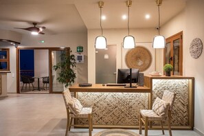A modern hotel lobby with a reception desk, two chairs, a ceiling fan, and a decorative wall panel. - Cretan Seaside Boutique Hotel (Hersonissos)