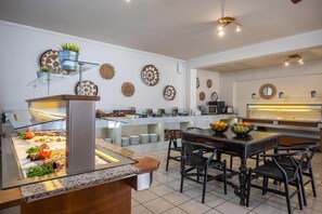 A buffet area with a variety of food options, a dining table with chairs, and decorative wall plates. - Cretan Seaside Boutique Hotel (Hersonissos)