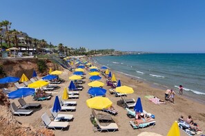 A beach with rows of sun loungers and umbrellas, a clear sky, and a calm sea. - Cretan Seaside Boutique Hotel (Hersonissos)