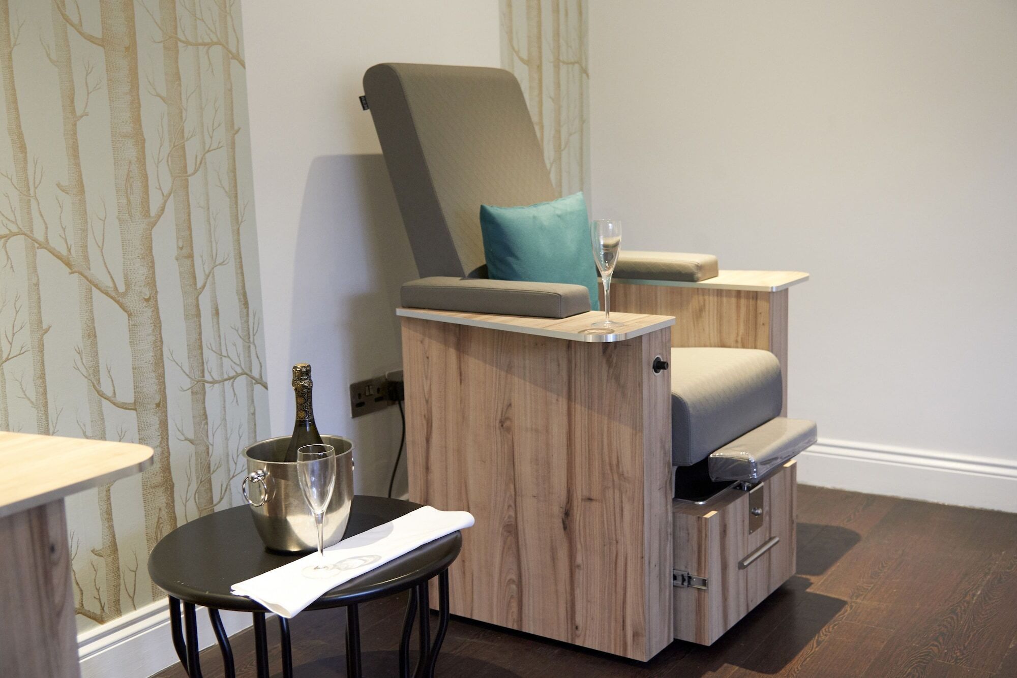 A massage chair with a footrest, a small table with a glass of champagne, and a bottle of champagne.