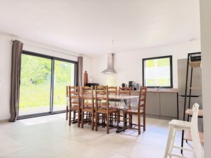 A dining area with a table and chairs, a kitchen with appliances, and a sliding glass door to the outdoors. - Les Lavandières - Collection La 21ème Planche (Barbeville)