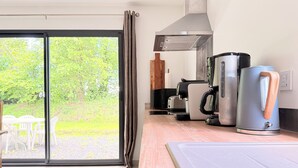 Ett modernt kök med en skjutdörr i glas som leder ut till en trädgård, en kaffemaskin och en vattenkokare på köksbänken.