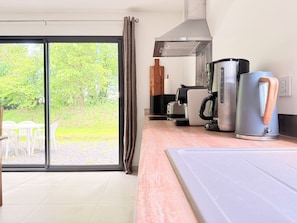 A modern kitchen with a sliding glass door to a garden, a coffee machine, and a kettle on the counter. - Les Lavandières - Collection La 21ème Planche (Barbeville)