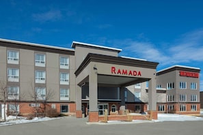 Ein mehrstöckiges Hotel mit einem gut sichtbaren 'RAMADA'-Schild, einem überdachten Eingang und einem Schild mit der Aufschrift 'WATERSLIDE' auf der rechten Seite.