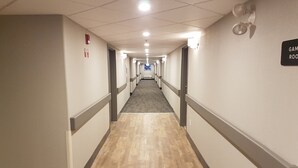 A hotel hallway with a carpeted floor, a fire alarm on the left wall, and a sign indicating the direction to the game room. - Ramada Cochrane (Cochrane)