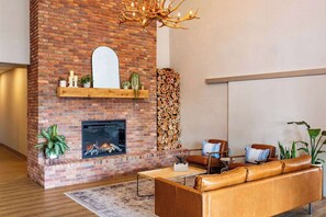 A modern living room with a brick fireplace, leather sofa, and a large mirror. - Ramada Cochrane (Cochrane)