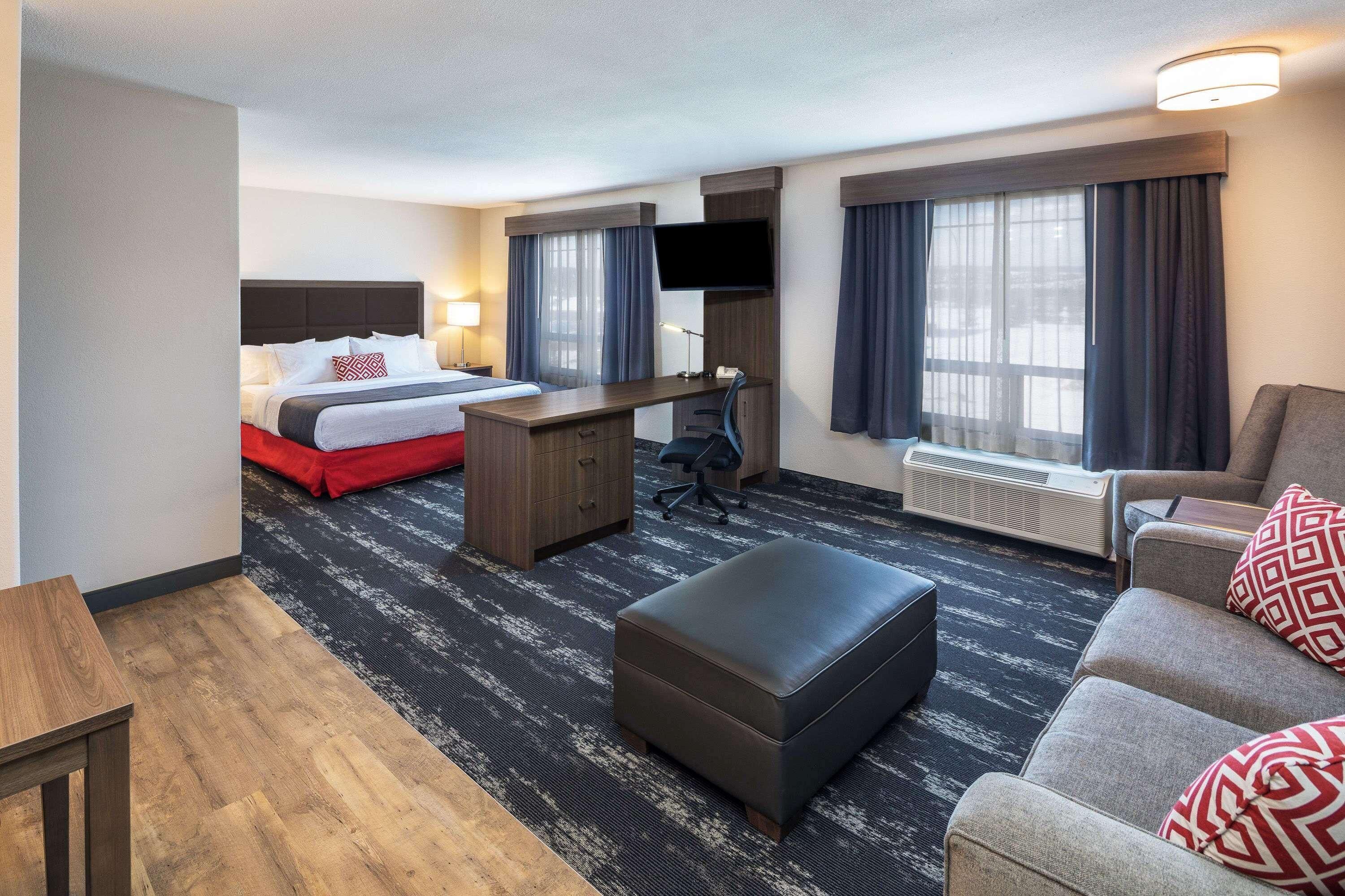 A hotel room with a bed, desk, chair, ottoman, and a sofa.