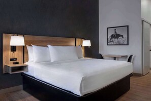 A modern hotel room with a large bed, two bedside tables with lamps, a small table, and a chair. - Ramada Cochrane (Cochrane)