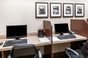 Un espacio de trabajo con dos monitores, un teclado, un ratón, un teléfono y un marco de fotos en la pared.