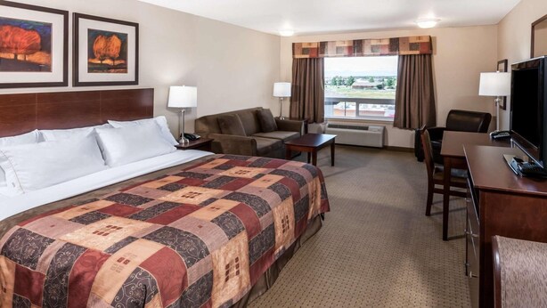 Quarto de hotel com uma cama grande, uma escrivaninha, uma cadeira, uma televisão e duas quadros na parede.