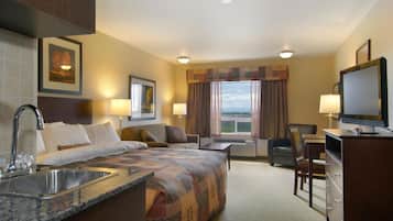 Habitación de hotel con cama, escritorio, televisión, lavabo y ventana con cortinas.