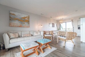Ein Wohnzimmer mit einer Couch, einem Couchtisch, Korbstühlen, einem Esstisch und einer Küche im Hintergrund.
