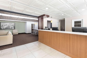 Una zona reception con un bancone in legno, un divano bianco, un tappeto decorato e un soffitto con motivo geometrico.