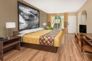 Una camera d'albergo con un letto grande, una scrivania, una sedia, una TV e una finestra con tende.