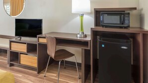 A hotel room with a desk, a television, a lamp, a microwave, and a refrigerator. - Asheville Airport Inn (Fletcher)