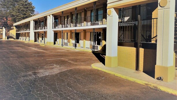 A hotel with a row of rooms, a parking lot, and a clear sky. - Asheville Airport Inn (Fletcher)