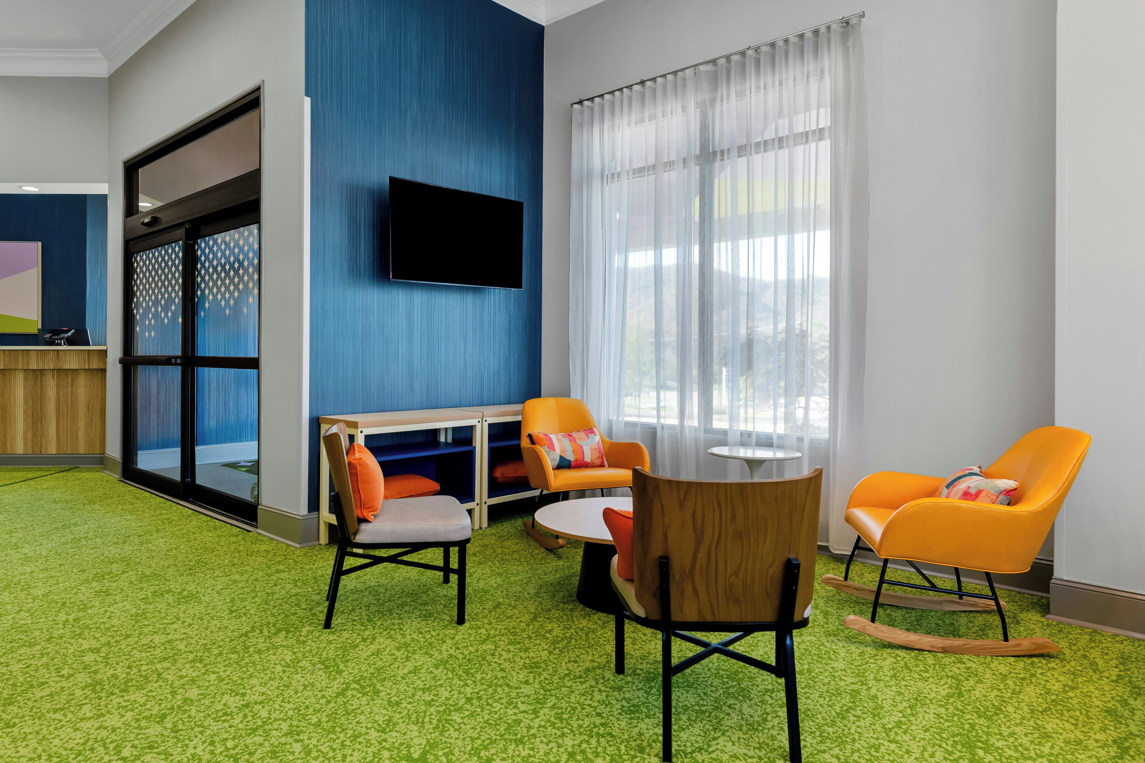 A modern room with a flat-screen TV mounted on the wall, a glass door leading outside, and a green carpet.