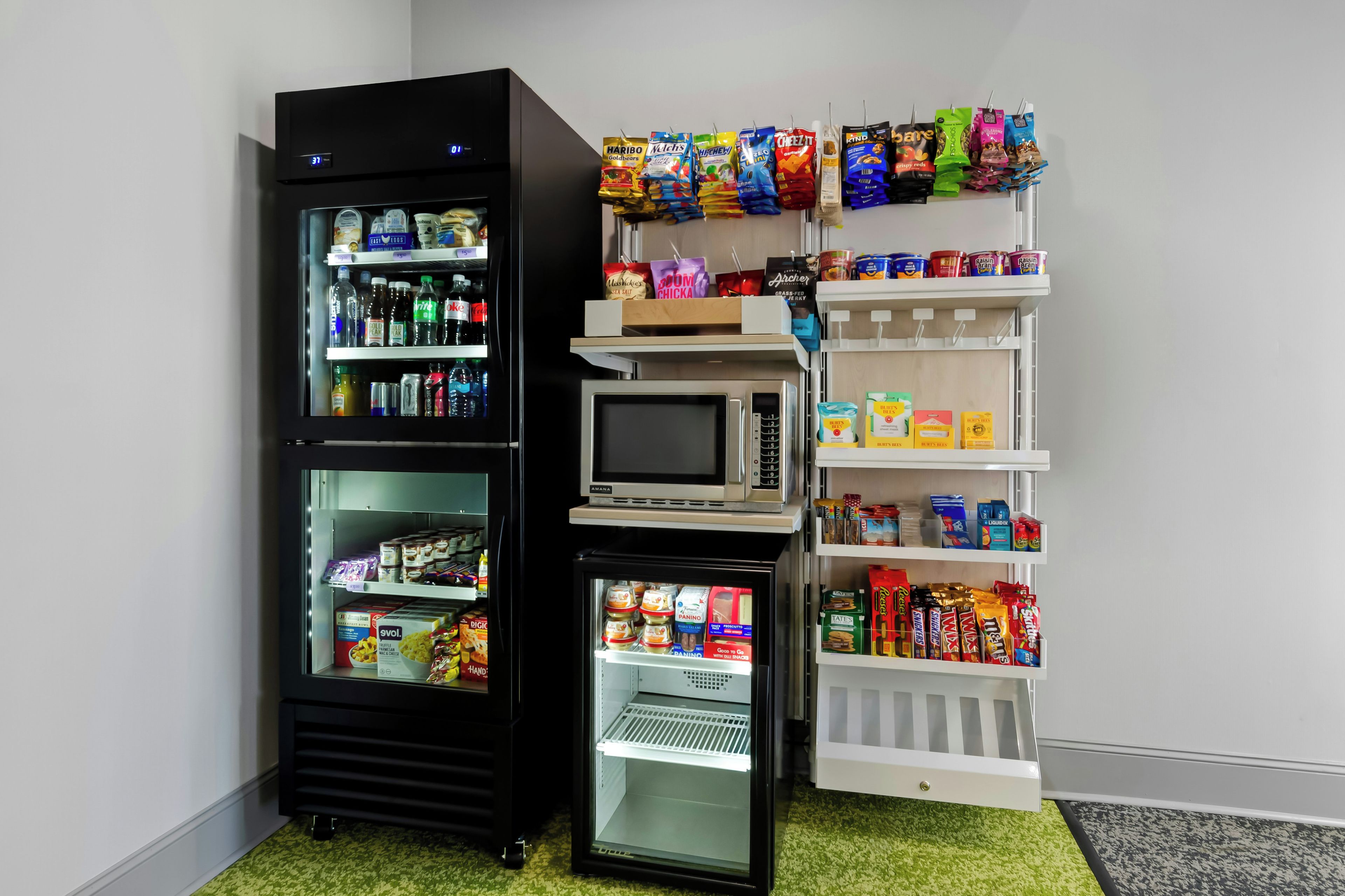 Une petite cuisine équipée d’un réfrigérateur, d’un four à micro-ondes et d’une petite étagère contenant des collations et des condiments.
