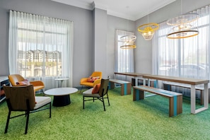 Un área de estar moderna con asientos, una mesa larga y ventanas grandes.