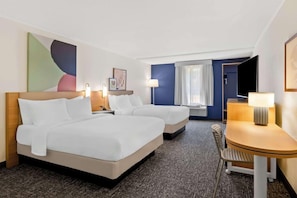 Quarto de hotel com duas camas, uma escrivaninha, uma cadeira, uma televisão e uma janela com cortinas.