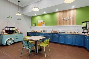 A modern cafe interior with a green accent wall, a coffee station, and a seating area with colorful chairs.