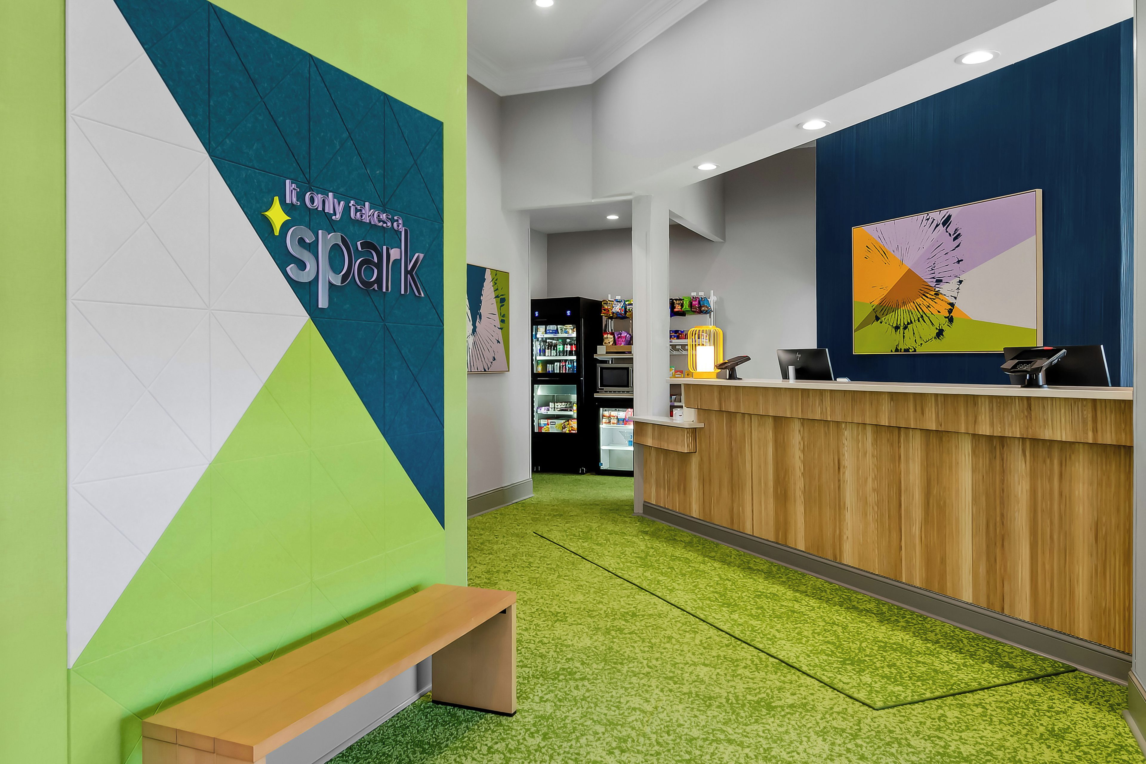 Zona de recepción con mostrador de madera, una banca y pared con diseño geométrico y texto.