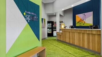 Zona de recepción con mostrador de madera, una banca y pared con diseño geométrico y texto.