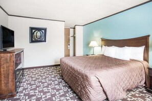 Une chambre d’hôtel comprenant un lit, une télévision, une œuvre d’art accrochée au mur, un tapis à motifs et une table de chevet avec une lampe.