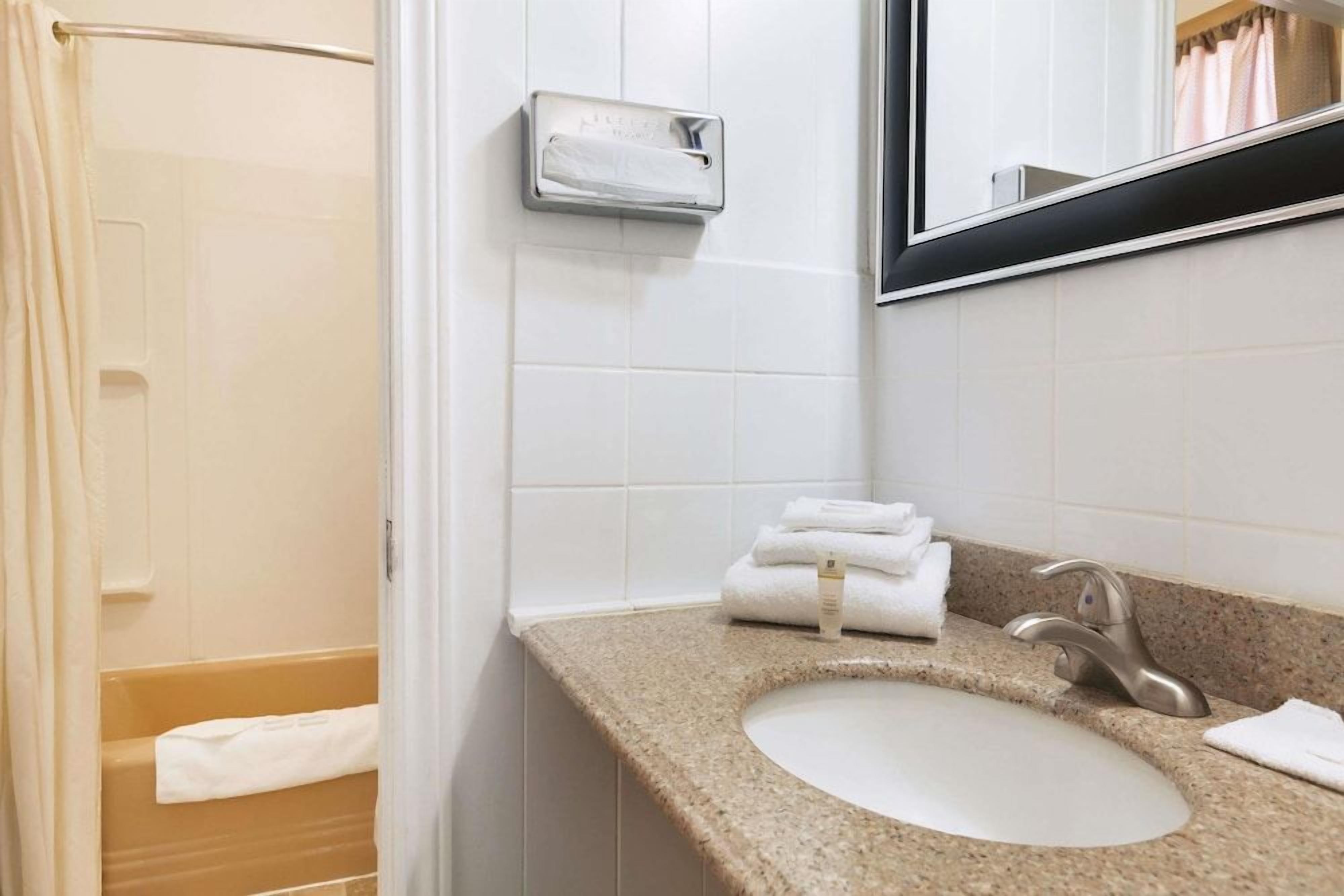 Une salle de bain équipée d’un lavabo, d’un miroir, d’un distributeur de serviettes et d’un rideau de douche.
