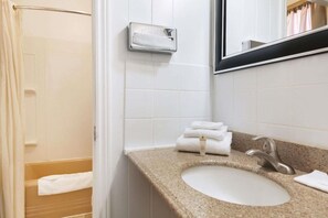 A bathroom with a sink, mirror, towel dispenser, and a shower curtain.