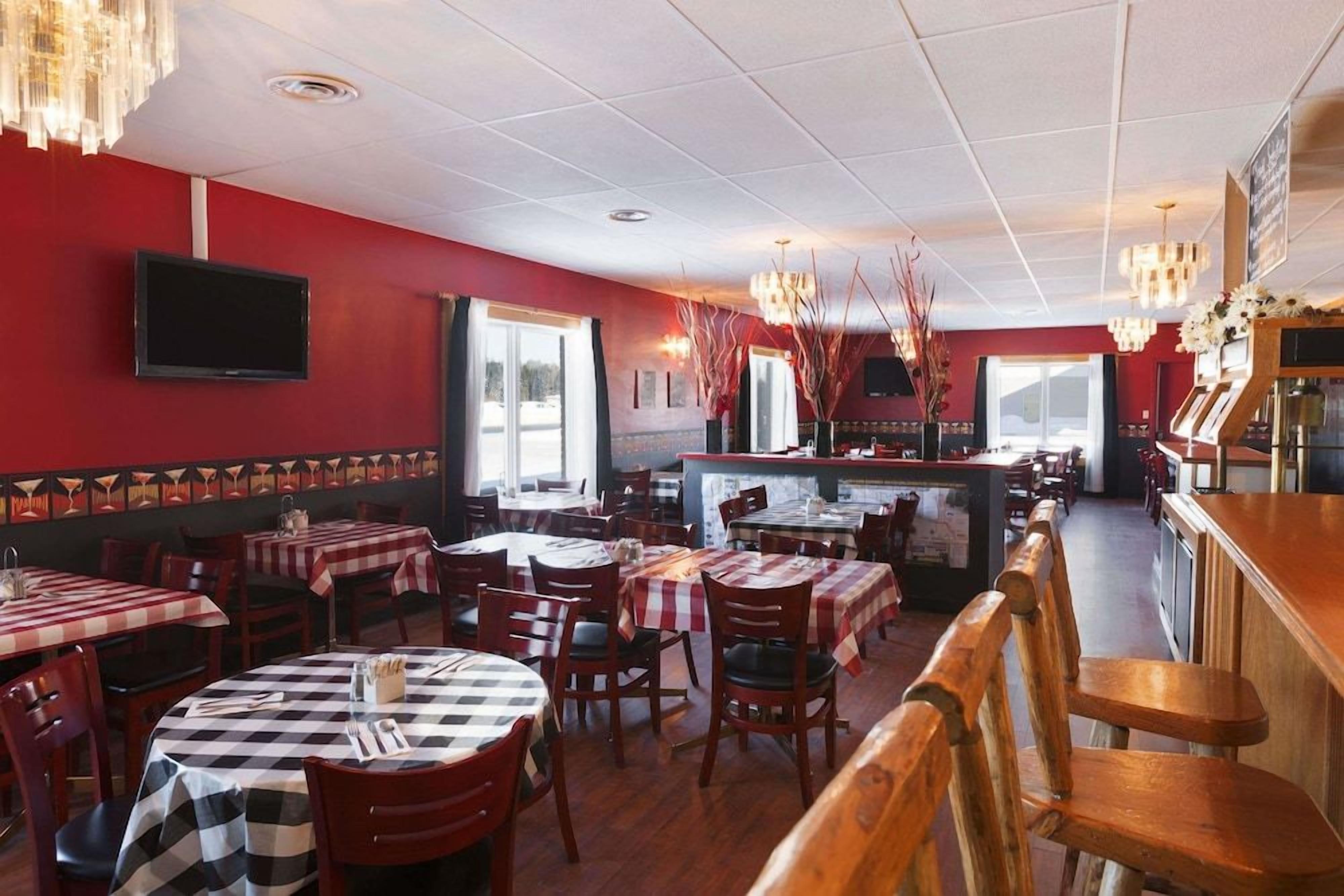 L’intérieur d’un restaurant avec des murs rouges, de nombreuses tables recouvertes de nappes à carreaux, des chaises en bois et un coin bar.